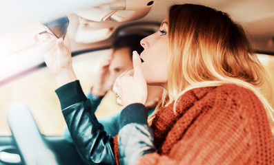 Woman watching her makeup in the mirror while driving a car. Dan