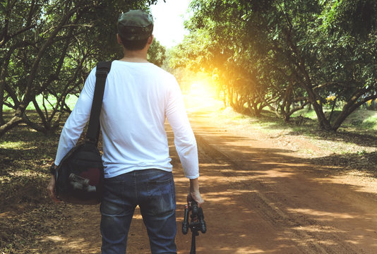 Enjoying travel. Back view Young man with backpack holding camera on walk away ground.