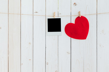 Red heart and photo frame blank hanging at clothesline on wood w