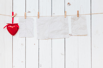 Red heart and old paper blank hanging at clothesline on wood whi
