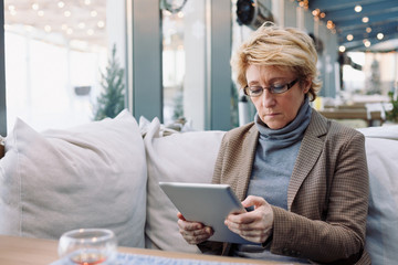 Mid age woman with tablet sitting at indoor cafe looking for screen