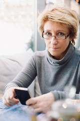 Mid age woman with cell phone sitting at indoor cafe looking in camera