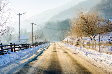 Frosted road in a rural village on a sunny bright winter day with snow all over the fences and...