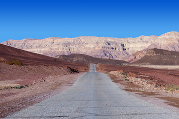 Empty desert road with mountains and blue sky in the background