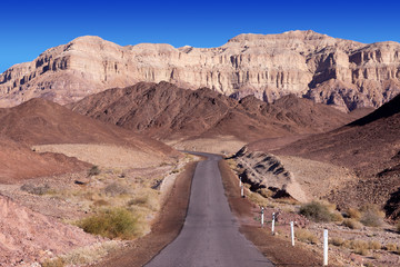 Empty desert road with mountains and blue sky in the background