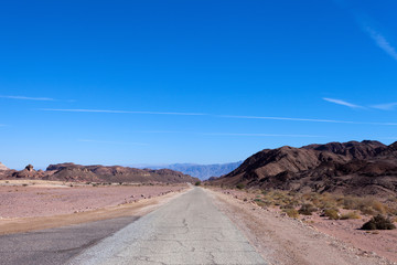 Empty desert road with mountains and blue sky in the background