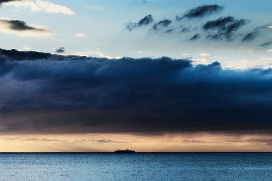 Cloudscape with huge dramatic dark nimbostratus cloud formation over Baltic sea and small silhouette of container ship on the horizon. Pomerania, Poland.