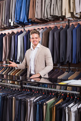 Man seller displaying diverse suits in men’s cloths store