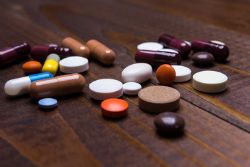 Pills of different colors and shapes on a background of brown wooden table