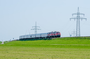 German train driving on Hindenburg Dam towards the island Sylt with green grass and electricity poles, Germany