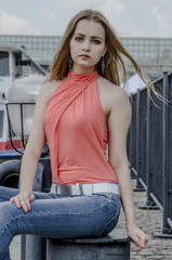 Young beautiful blonde girl in a red summer blouse and jeans posing flexible 
on the pier at the river bank

