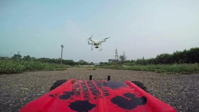 RC cars with a camera rides on the dirt road and filmed the quadrocopter, flying in front of the car.
