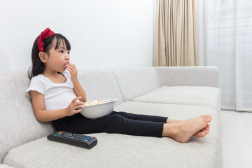 Obraz premium Happy Asian Chinese little girl eating popcorn on the sofa