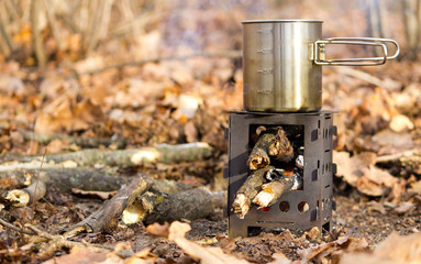 Tourist travel mini stove with tea in steel handle mug in the autumn forest