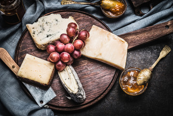 Cheese on rustic wooden Plate with knife, spoon and sauces, top view. Dark style