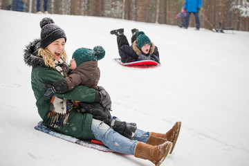 Mother and little toddler boy sliding down the hill in the winter forest and having fun with snow....