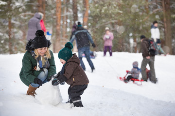 Cute little toddler boy and his mother playing with snow and making snowman. Child having fun outdoors in winter.