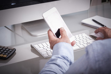 Geschäftsmann im Büro mit Smartphone am Schreibtisch, anonym v