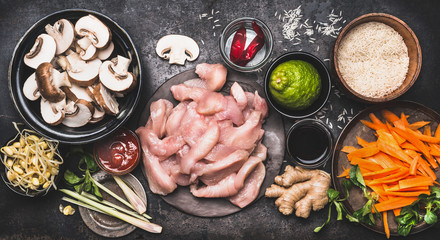 Food ingredients for asian cooking with rice, chicken ,vegetables and spices in bowls, top view