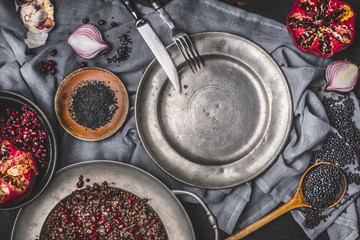 Healthy vegetarian black lentil salad with pomegranate on kitchen table with empty plate and cutlery , top view. Country dark style