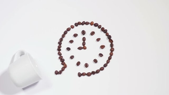Clock made of coffee beans on white surface, nine o'clock is time for coffee, white cup appears and all roasted beans move inside cup. Stop motion. Close up, 4K Ultra HD.