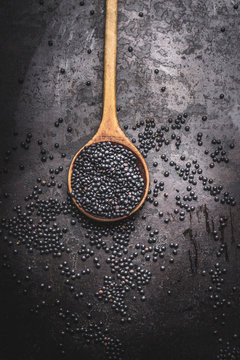 Black beluga lentil  seeds in wooden cooking spoon on dark rustic background, top view