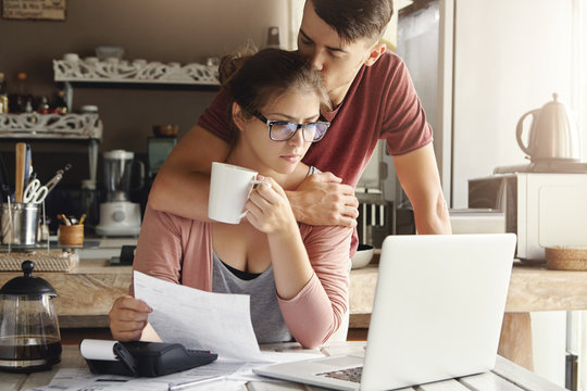 Unhappy Caucasian Family Having Economic Trouble, Not Able To Pay Out Debts. Supportive Young Man Trying To Cheer Up His Worried Wife In Glasses Who Is Feeling Stressed, Facing Financial Problem