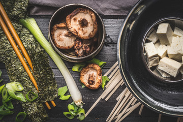Cooking ingredients for asian soup: udon noodls, tofu,  Shiitake Mushrooms , nori and green onion on dark rustic background, top view