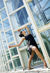   Woman standing in dance pose  on the building background, on the street.
