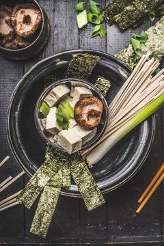 Asian soup preparation in bowl with udon noodls, tofu,  Shiitake Mushrooms , nori and green onion on dark rustic background, top view