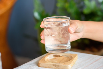 Hand of woman holding glass of drinking water with ice