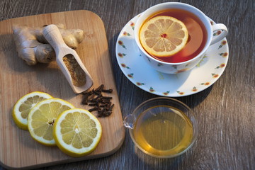 A cup of tea with honey and lemon next to ginger root, cloves and lemon slices