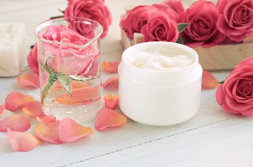Obraz na płótnie Canvas Jar of facial anti-age cream, infused floral attar in glass test vial, fresh roses, pink petals, white wooden table. Soft focus, toned. 