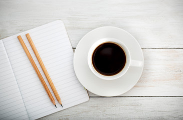 white desk with cup of coffee,pencil; notebook. lay flat