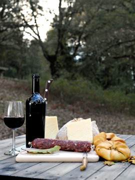 Outdoor eating with bread, cheese, sausage and red wine.