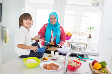 Muslim traditional woman with little son in modern white kitchen