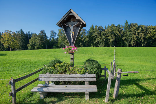 Marterl mit Jesus-Figur und Holzbank