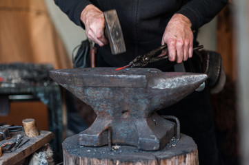 Blacksmith at the workshop. Working metal with hammer and tools on the anvil in the forge.