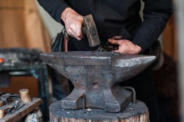 Blacksmith at the workshop. Working metal with hammer and tools on the anvil in the forge.