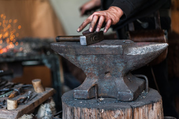 Blacksmith at the workshop. Working metal with hammer and tools on the anvil in the forge.