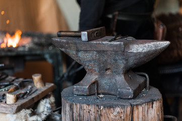 Blacksmith at the workshop. Working metal with hammer and tools on the anvil in the forge.