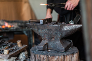 Blacksmith at the workshop. Working metal with hammer and tools on the anvil in the forge.