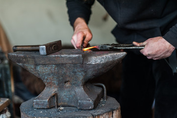 Blacksmith at the workshop. Working metal with hammer and tools on the anvil in the forge.