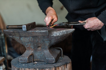 Blacksmith at the workshop. Working metal with hammer and tools on the anvil in the forge.