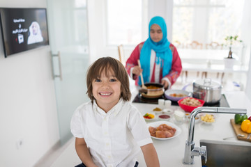 Muslim traditional woman with little son in modern white kitchen