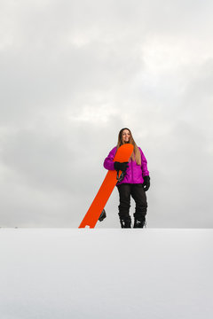 Young woman and her orange snowboard on a snow-covered mountainside
