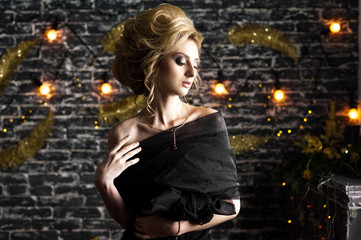 Fototapeta premium beautiful young blond woman with gorgeous hair in a black dress on a background of gray brick with bokeh