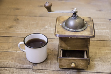 Vintage manual coffee grinder and a cup of coffee on a wooden su
