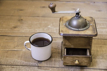 Vintage manual coffee grinder and a cup of coffee on a wooden su