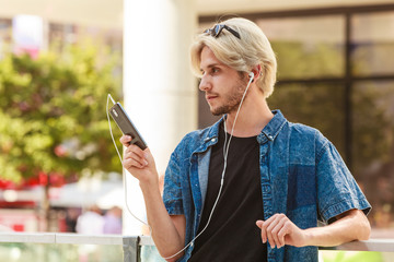 Hipster man standing on city street listening music
